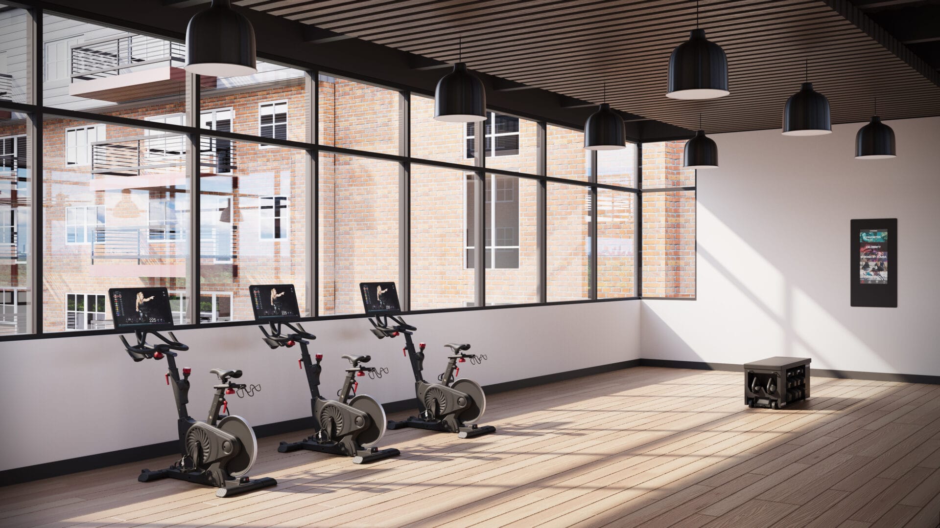 A gym with three stationary bikes and two windows.